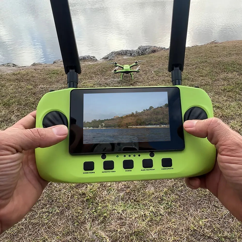Person holding Xpece remote controller with live video view, drone on grass near a lake