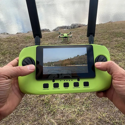 Person holding Xpece remote controller with live video view, drone on grass near a lake